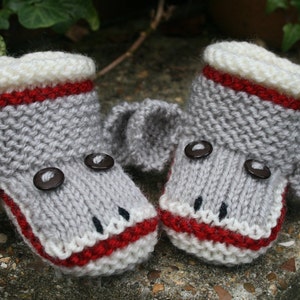 May include: A pair of gray knitted baby booties with red and white trim, shaped like monkeys with black button eyes.