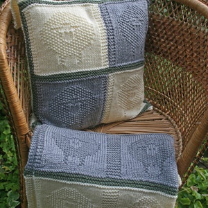 May include: A knitted cushion with a geometric pattern in shades of white and grey. The cushion is sitting on a wicker chair.