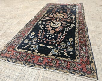 Puede incluir: Una alfombra rectangular con un campo central de color azul marino oscuro con intrincados motivos florales y botánicos en tonos salmón, crema y azul claro. La alfombra está enmarcada por un borde ancho con un patrón floral repetitivo en rojo y beige.