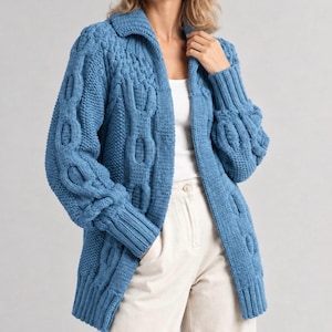 Puede incluir: Un cárdigan de punto grueso en color azul brillante con un patrón de trenzas prominente, cuello ancho y mangas largas con puños acanalados. La prenda se lleva sobre una camiseta sin mangas blanca y pantalones claros, mostrando su textura.