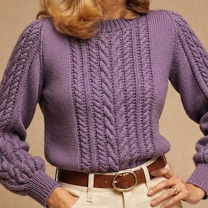 May include: A lavender long-sleeve jumper featuring a vertical cable knit pattern on the front and sleeves, a round neckline, and ribbed cuffs. The jumper is tucked into light-coloured trousers secured with a brown leather belt with a gold buckle.