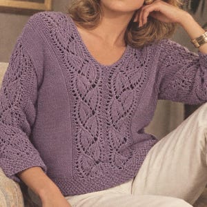 May include: A lavender long-sleeve jumper featuring a V-neckline and intricate openwork knit patterns. The design includes vertical columns of leaf-shaped lace motifs along the centre front and sleeves, complemented by solid knit side panels.