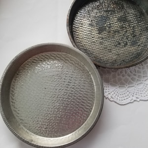 May include: Two silver metal cake pans with a textured surface. The pans are labeled "Cake King" and "Cake King" with the words "Made in USA" printed below.