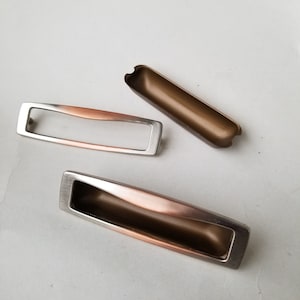 May include: Two cabinet pulls with a brushed nickel finish and a copper accent. The pulls are rectangular with a recessed center.