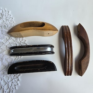 May include: A collection of vintage wooden drawer pulls and handles in various shapes and finishes. Includes a light brown, oval-shaped pull, a black and silver handle, and several dark brown wooden pulls. Ideal for antique furniture restoration.
