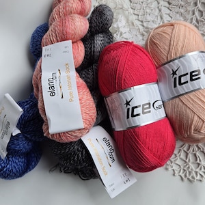May include: A selection of yarn skeins in various colours, including red, peach, grey, and blue. The yarn is labelled with brand and colour information. The image displays a range of textures and shades, suitable for knitting or crochet projects.