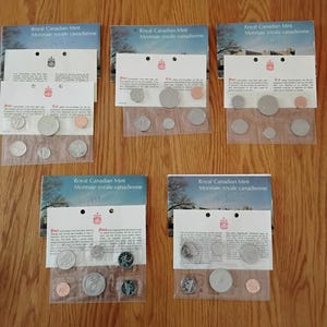 May include: Five Royal Canadian Mint coin sets, each in a clear plastic sleeve with a white card. The cards display "Royal Canadian Mint Monnaie royale canadienne" and the year 1974. The coins are of various sizes and colours.