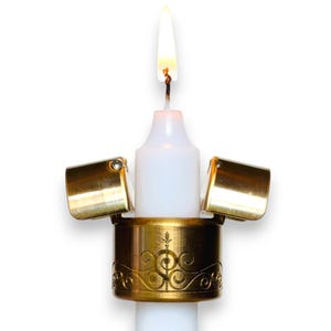 May include: A lit white candle with a gold-colored candle snuffer. The snuffer is attached to a decorative gold base with an ornate design. The candle flame is bright and the background is white.