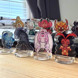 May include: A collection of acrylic character standees featuring various cartoon characters. The standees are colorful and detailed, with clear bases for display. The characters have unique designs and expressions, suitable for collectors.
