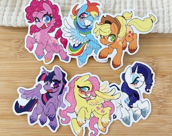 May include: A set of six die-cut vinyl stickers featuring cartoon ponies in various colors including pink, blue, orange, purple, yellow, and white. Each pony character displays distinct features such as wings, horns, and unique cutie marks.