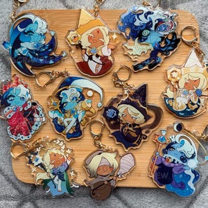 Puede incluir: Una colección de diez llaveros de acrílico transparente con coloridas ilustraciones de personajes estilo anime y cierres de mosquetón de metal dorado. Cada llavero muestra un diseño de personaje único con atuendos, accesorios y paletas de colores distintos.
