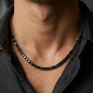 May include: A black necklace with square-cut stones is displayed against a dark background. The necklace is worn over a dark gray button-down shirt. The brand "VALLEA JEWELRY" is visible in the upper left corner.