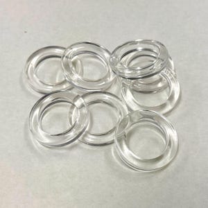 Op de afbeelding: Een verzameling heldere, transparante acrylringen. De ringen zijn cirkelvormig met een gladde, gepolijste afwerking. Ze zijn licht overlappend gerangschikt, waardoor een gevoel van diepte ontstaat. Geschikt voor diverse knutsel- en designprojecten.