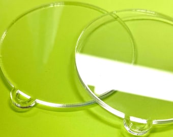 May include: Two transparent, circular acrylic pieces with a small, curved handle on the edge. The clear objects overlap against a bright green background, creating light and shadow. The design suggests a focus on clarity and simplicity.