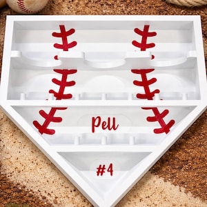 Puede incluir: Expositor blanco con forma de base de béisbol, con detalles de costuras rojas. El nombre "Pell" y el número "4" se muestran en rojo. Una pelota de béisbol y bates en el fondo.