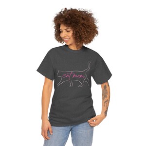 Puede incluir: Camiseta gris oscuro con un contorno rosa de gato y la frase "cat mom" en cursiva. La camiseta tiene cuello redondo y está hecha de un tejido suave, ideal para uso diario.