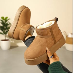 Puede incluir: Botines marrones con forro de piel sintética. Las botas tienen una suela gruesa de color marrón claro y un exterior similar al ante. El interior está forrado con suave piel sintética blanca. Botas de invierno.