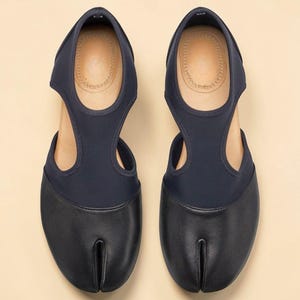 May include: A pair of navy blue split-toe shoes. The shoes have a leather toe section and a fabric upper with a cutout design. The insoles are tan. The shoes are designed to be worn with a separate big toe compartment.