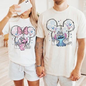 Puede incluir: Dos camisetas de manga corta en color blanco roto con estampados gr&aacute;ficos de personajes Disney. Una muestra un personaje rosa con lazo dentro de una silueta de orejas de Mickey, la otra un personaje azul dentro de un contorno similar.