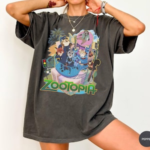 Puede incluir: Camiseta gris oscuro con un gr&aacute;fico colorido de la pel&iacute;cula animada "Zootr&oacute;polis". El dise&ntilde;o incluye varios personajes de animales y el t&iacute;tulo de la pel&iacute;cula en una fuente vibrante y multicolor. La camiseta tiene un corte holgado y mangas cortas.