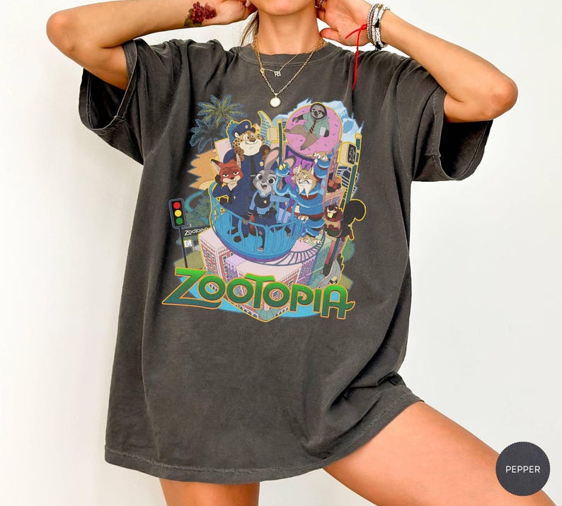 Puede incluir: Camiseta gris oscuro con un gr&aacute;fico colorido de la pel&iacute;cula animada "Zootr&oacute;polis". El dise&ntilde;o incluye varios personajes de animales y el t&iacute;tulo de la pel&iacute;cula en una fuente vibrante y multicolor. La camiseta tiene un corte holgado y mangas cortas.