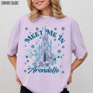 May include: A light purple t-shirt with the words "Meet Me In Arendelle" and a graphic of a castle, mountains, and snowflakes. The shirt is a Comfort Colors brand.