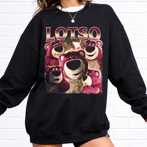 May include: Black sweatshirt featuring a graphic of Lotso, the bear character from Toy Story, with the word "LOTSO" in gold lettering. The image shows Lotso's face and other bears in shades of pink and white.