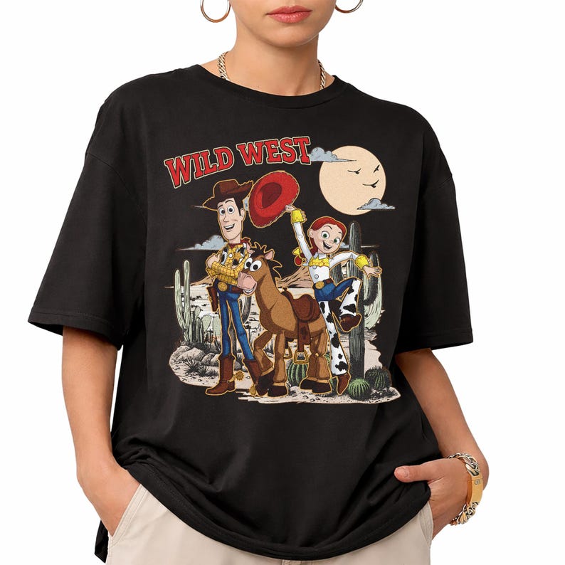 Pu&ograve; includere: T-shirt nera con un design del West selvaggio con personaggi dei cartoni animati. Il design include Woody, Jessie, un cavallo, un paesaggio desertico, un sole e il testo "WILD WEST" in rosso.
