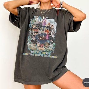 May include: Dark gray oversized t-shirt featuring a colorful graphic of cartoon characters. The shirt has the text "we're wild and we can't be tamed" in a rainbow font. The shirt has short sleeves and a relaxed fit.
