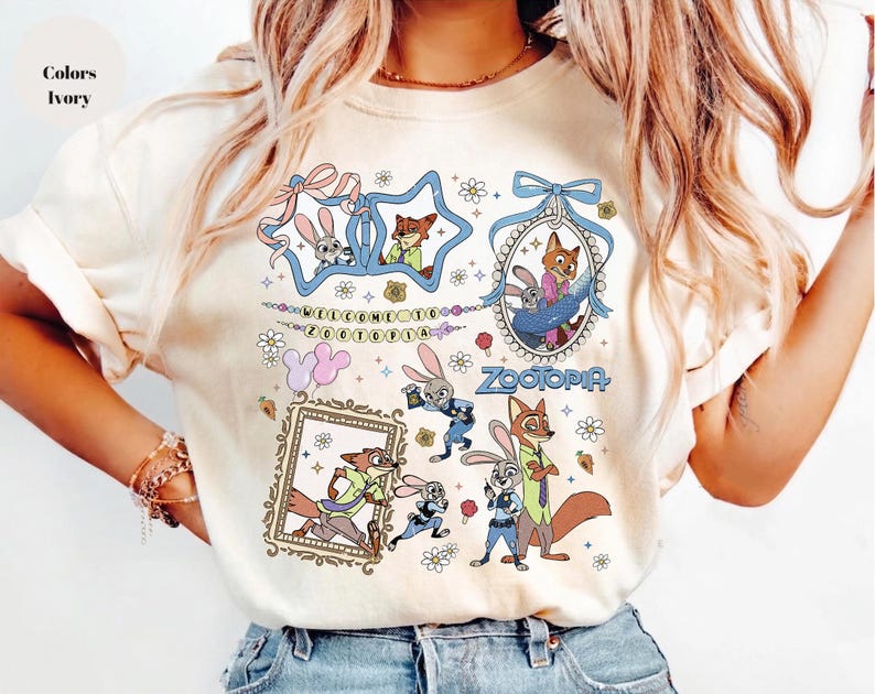May include: An ivory t-shirt featuring a graphic print of Zootopia characters Judy Hopps and Nick Wilde. The design includes multiple illustrations of the characters, floral accents, bows, and the text Welcome to Zootopia and Zootopia.