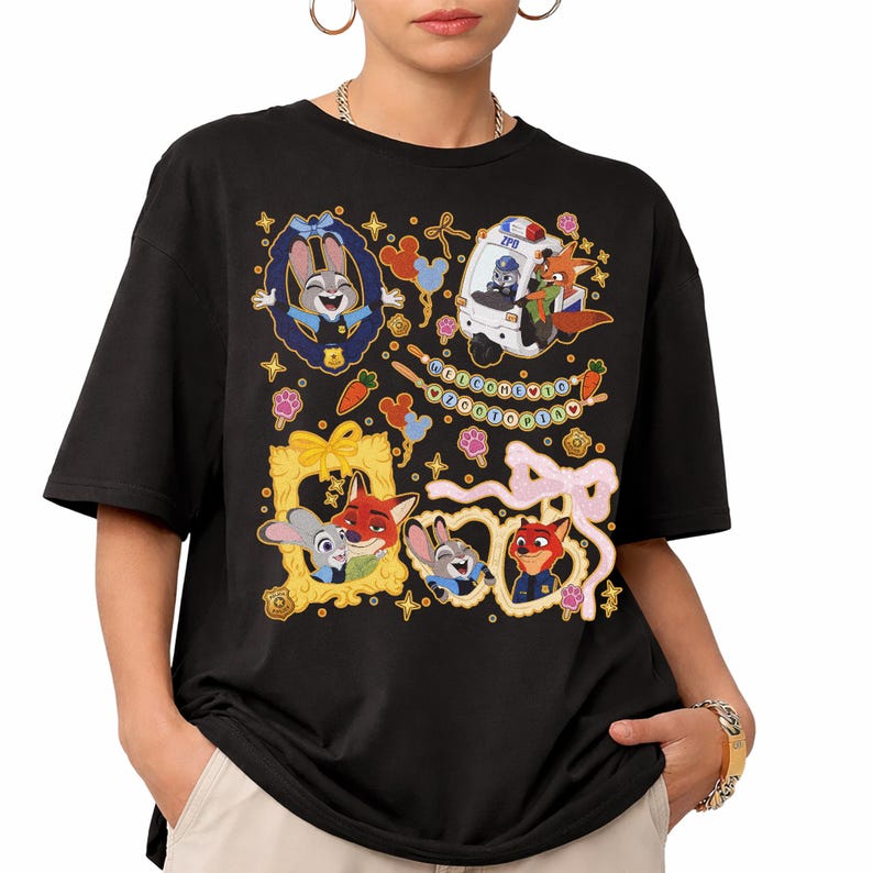 May include: Black t-shirt featuring colorful cartoon characters and decorative elements. The design includes framed images of a bunny and fox, a police vehicle, and the text "WELCOME TO Zootopia". The shirt has short sleeves and a relaxed fit.
