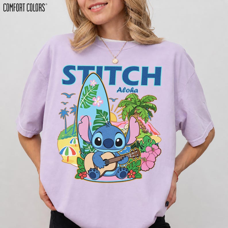 May include: A light purple t-shirt with a graphic of Stitch playing a ukulele in front of a surfboard, palm trees, and flowers. The word "STITCH" is above the graphic in blue letters, with "Aloha" below.