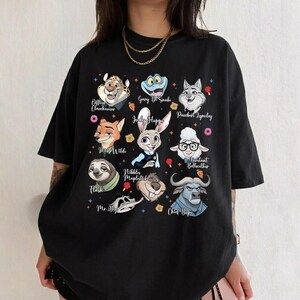 May include: A black short-sleeved t-shirt featuring a graphic print of various animated animal characters from Zootopia, including Judy Hopps, Nick Wilde, Flash, and Chief Bogo, with their names printed in white script text alongside small colorful icons.