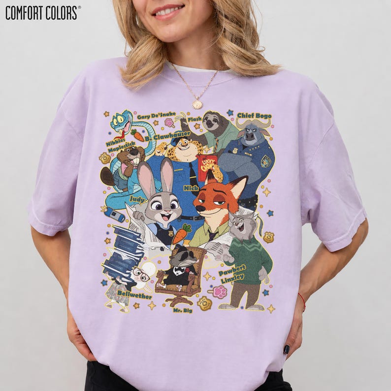 Op de afbeelding: Een lichtpaars Comfort Colors T-shirt met een kleurrijke afbeelding van personages uit de film Zootopia, waaronder Judy Hopps en Nick Wilde. Het ontwerp toont verschillende personages uit de film. Het T-shirt heeft korte mouwen.