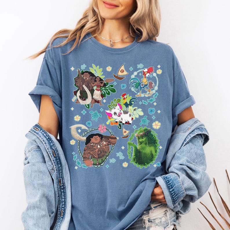 May include: Blue t-shirt featuring colorful cartoon characters from a popular animated movie. The design includes images of a woman, a rooster, a pig, and other tropical elements. The shirt is made of a soft material.