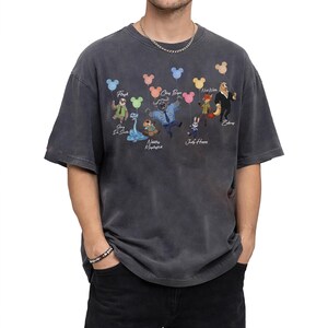 May include: A charcoal grey short-sleeve t-shirt featuring a graphic print of various animated animal characters from Zootopia, each holding a colourful balloon shaped like a mouse head. The names of the characters are printed below each figure.