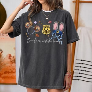 May include: A charcoal gray short-sleeve t-shirt featuring a graphic print of Zootopia-themed icons including a police badge, bunny ears, and a carrot. The text "Don't mess with the bunny" is printed in white script below the colorful illustrations.
