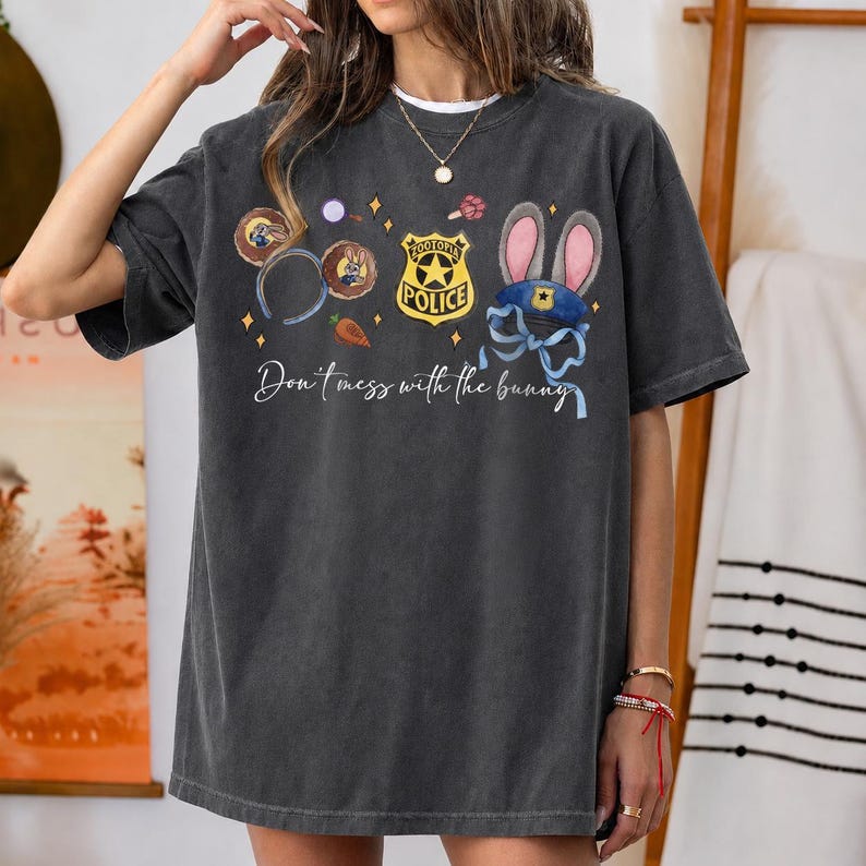 May include: A charcoal gray short-sleeve t-shirt featuring a graphic print of Zootopia-themed icons including a police badge, bunny ears, and a carrot. The text "Don't mess with the bunny" is printed in white script below the colorful illustrations.