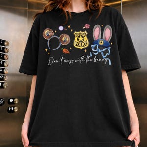 May include: A black short-sleeve t-shirt featuring a graphic print with Zootopia-themed icons including mouse ears, a police badge, a carrot, and a blue hat with rabbit ears. The text "Don't mess with the bunny" is printed in white script.
