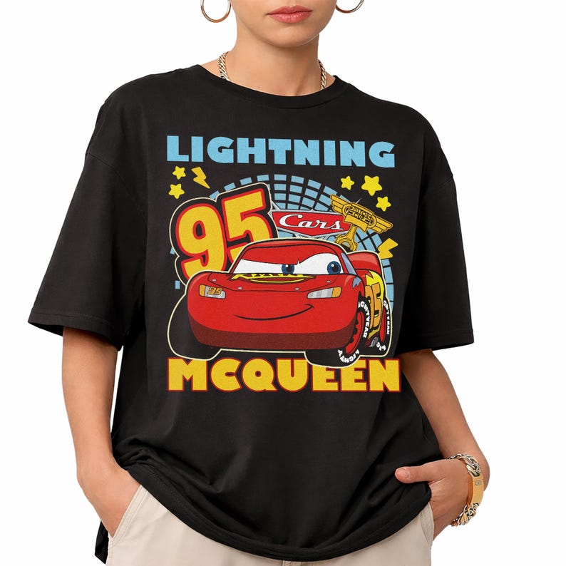 May include: Black t-shirt featuring a graphic of Lightning McQueen from the Cars movie. The design includes the number 95, stars, and the text "LIGHTNING" and "MCQUEEN" in yellow and blue. The shirt has short sleeves.