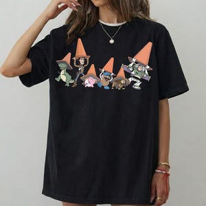 May include: Black t-shirt featuring a graphic of Toy Story characters wearing orange traffic cones. The characters include Rex, Woody, Hamm, Mr. Potato Head, Slinky Dog, and Buzz Lightyear. The shirt has a crew neck and short sleeves.