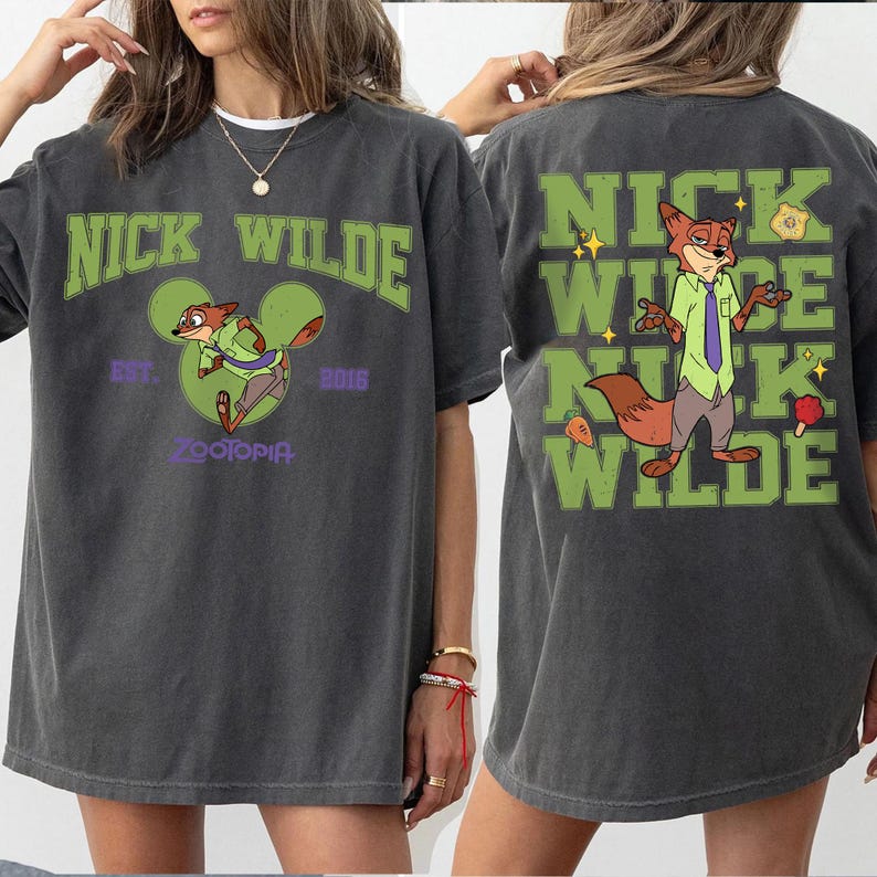 May include: A charcoal gray t-shirt featuring Nick Wilde from Zootopia. The front displays the text NICK WILDE, a green Mickey Mouse silhouette, and the text EST. 2016 ZOOTOPIA. The back shows a large graphic of Nick Wilde with the text NICK WILDE.