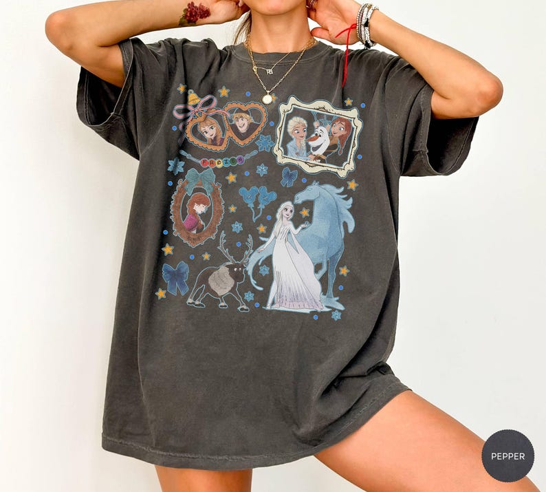 Puede incluir: Camiseta gris oscuro con un gr&aacute;fico colorido de personajes de la pel&iacute;cula animada Frozen. El dise&ntilde;o incluye im&aacute;genes de Elsa, Anna, Olaf y Sven, con detalles en azul y amarillo. La camiseta tiene un corte holgado.