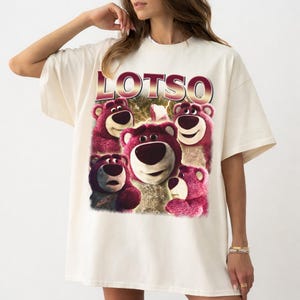 May include: Cream-colored t-shirt featuring a graphic of Lotso, the bear character from Toy Story. The word "LOTSO" is printed above the bear graphic in a red and pink gradient font. The graphic includes multiple images of Lotso.