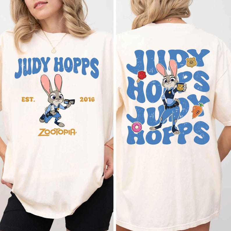 May include: An off-white t-shirt featuring Judy Hopps from Zootopia. The front displays the text Judy Hopps, Est. 2016, and Zootopia with a graphic of the rabbit character. The back shows a large repeating blue text design with Judy Hopps.