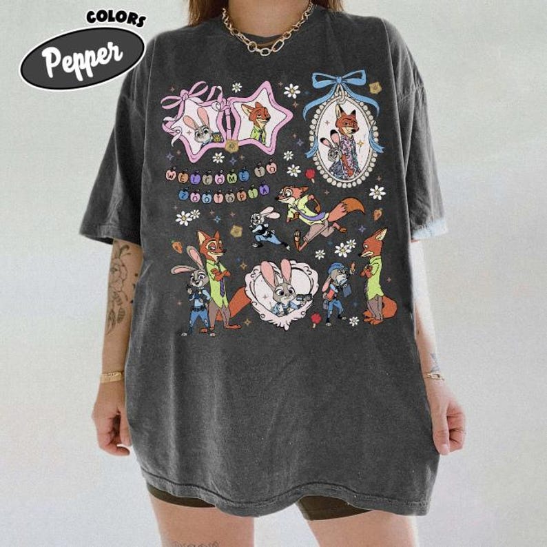 May include: A charcoal gray oversized t-shirt featuring a graphic print of characters from Zootopia, including Judy Hopps and Nick Wilde. The design includes floral accents, decorative frames, and the text Welcome to Zootopia in colorful letters.