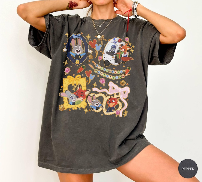 May include: Dark gray t-shirt featuring cartoon characters in gold frames, a police car, and decorative elements. The shirt has a relaxed fit and short sleeves. The design includes the text "Welcome to Zootopia".