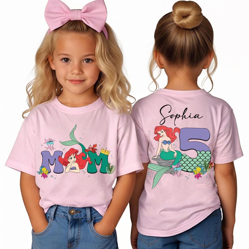 May include: Pink t-shirts with a Little Mermaid theme. The front of the shirt says "MOM" with Ariel illustrations. The back of the shirt has the name "Sophia" and a mermaid illustration with the number "5".
