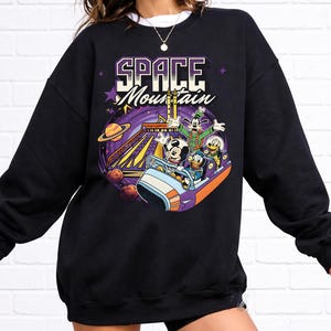 May include: Black sweatshirt with a vibrant graphic of Mickey Mouse, Goofy, Donald Duck, and Pluto on a Space Mountain ride. The words "SPACE MOUNTAIN" are printed above the characters in a purple and white font.