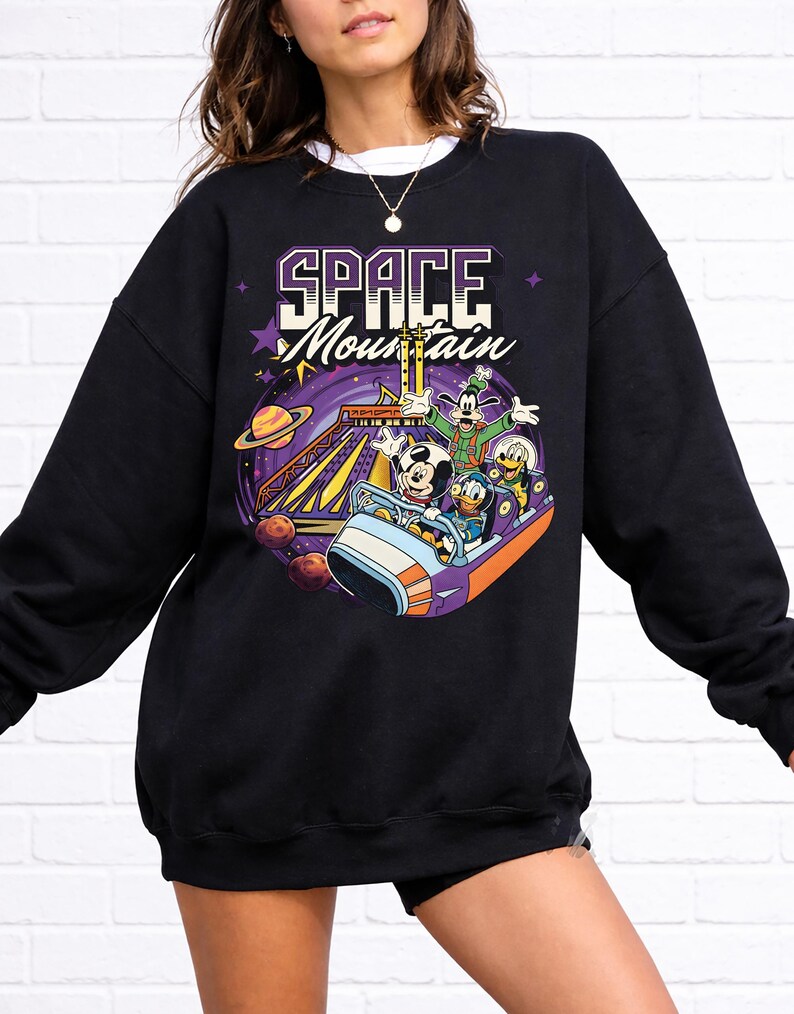 May include: Black sweatshirt with a vibrant graphic of Mickey Mouse, Goofy, Donald Duck, and Pluto on a Space Mountain ride. The words "SPACE MOUNTAIN" are printed above the characters in a purple and white font.